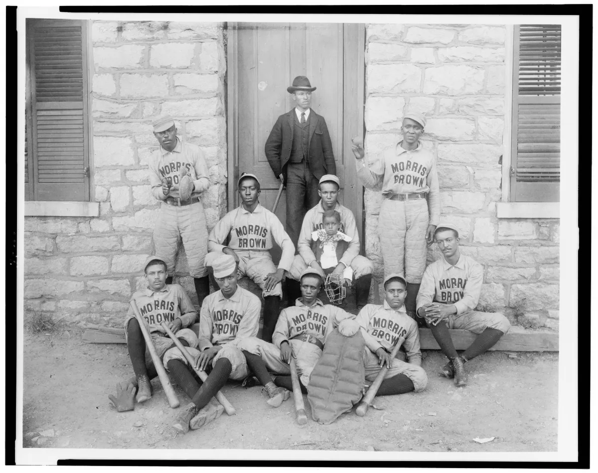 A group of African American baseball players from Morris Brown College in Atlanta, posed in front of a stone building, wearing their team uniforms with "Morris Brown" text.