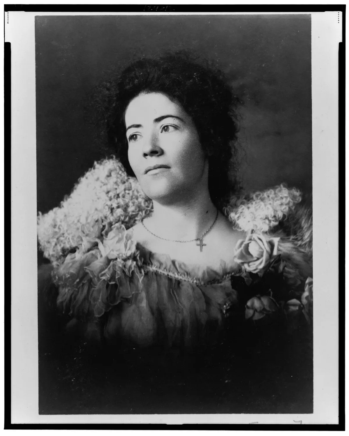 A formal portrait of a nursing student wearing a fur collar over a lace dress, with a floral brooch and a cross necklace.