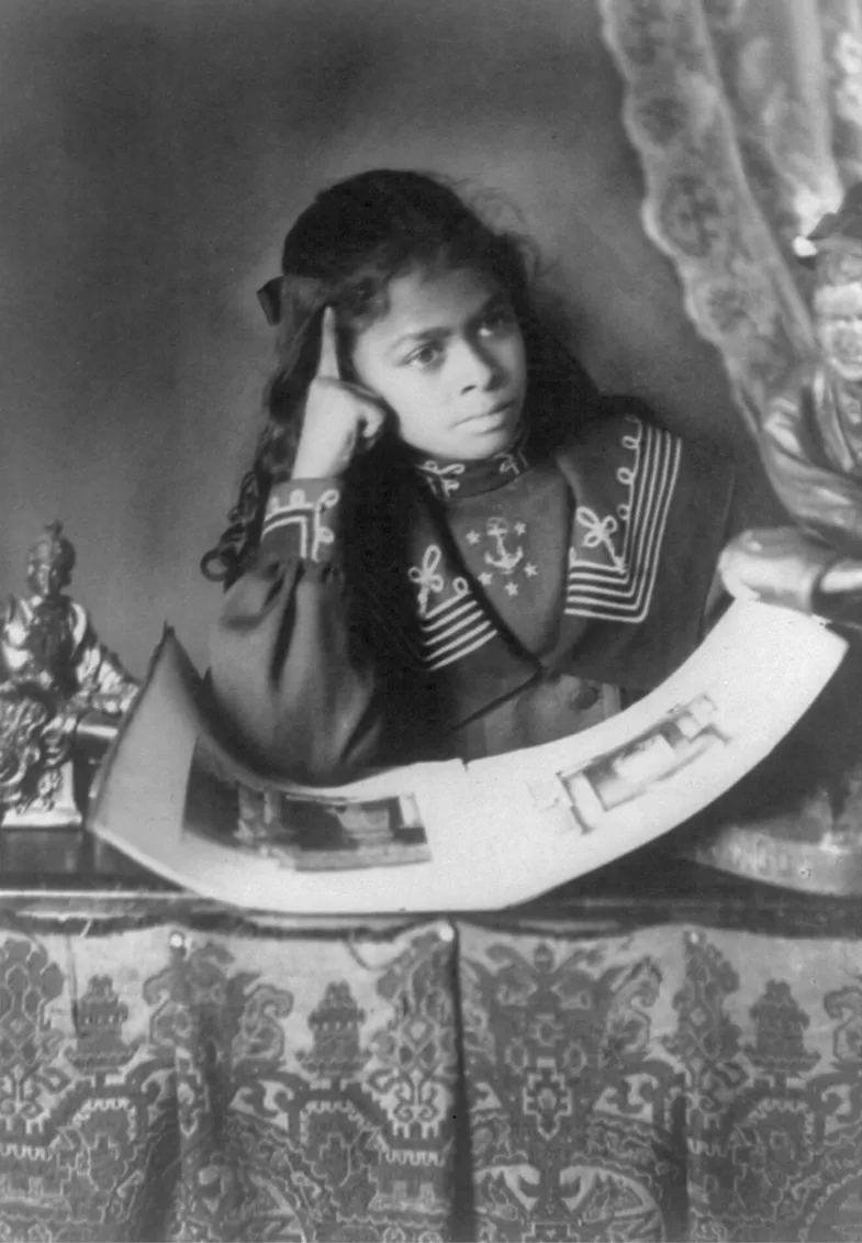 A young African American girl dressed in formal attire, seated at a brocade-covered desk, looking thoughtfully into the distance with her hand at her temple, surrounded by small statues.