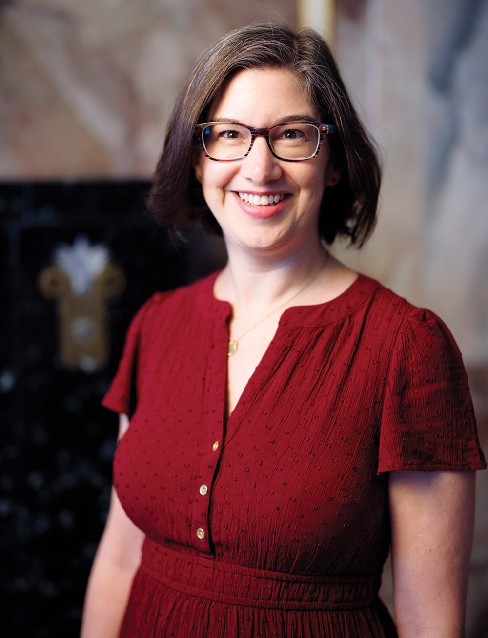 Aimee Hess wearing glasses in a crimson dress smiling.