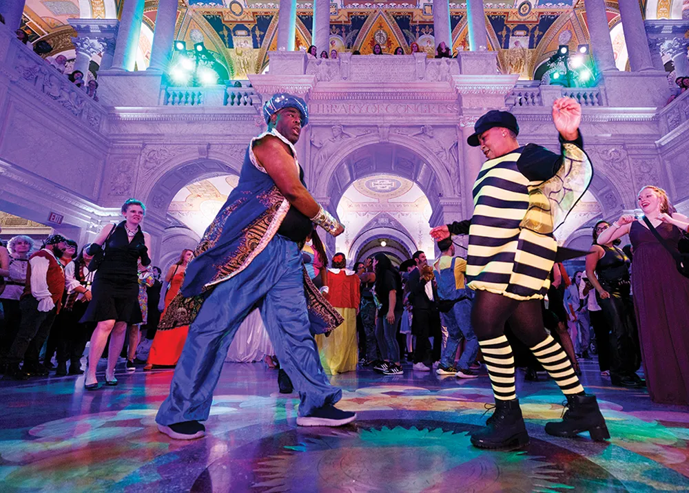 Two people dancing in costume inside a grand, ornate hall with a crowd in the background.