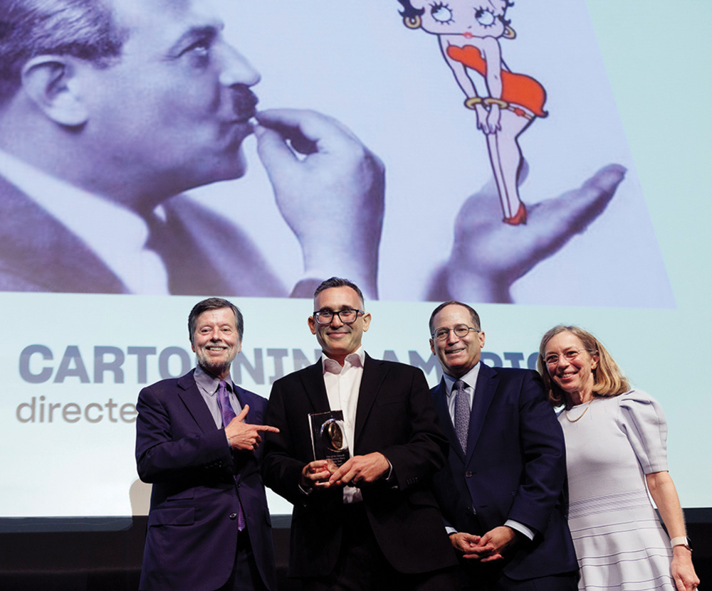 Four individuals stand in front of a backdrop featuring an image of a man holding Betty Boop. One holds an award.