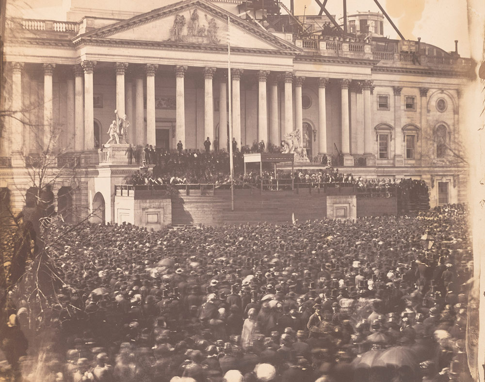 Historical photograph of a large crowd in front of a neoclassical building with columns.