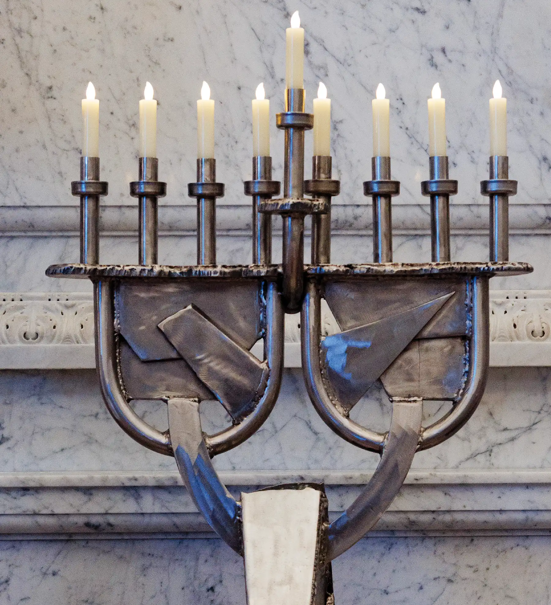 Metallic menorah with lit candles against a marble backdrop.