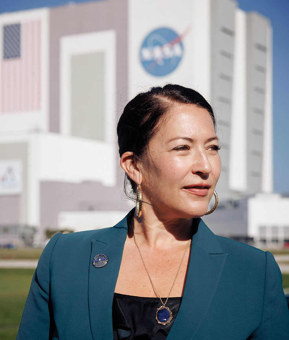 Ada Limón in a teal blazer stands in front of a building with a NASA logo.