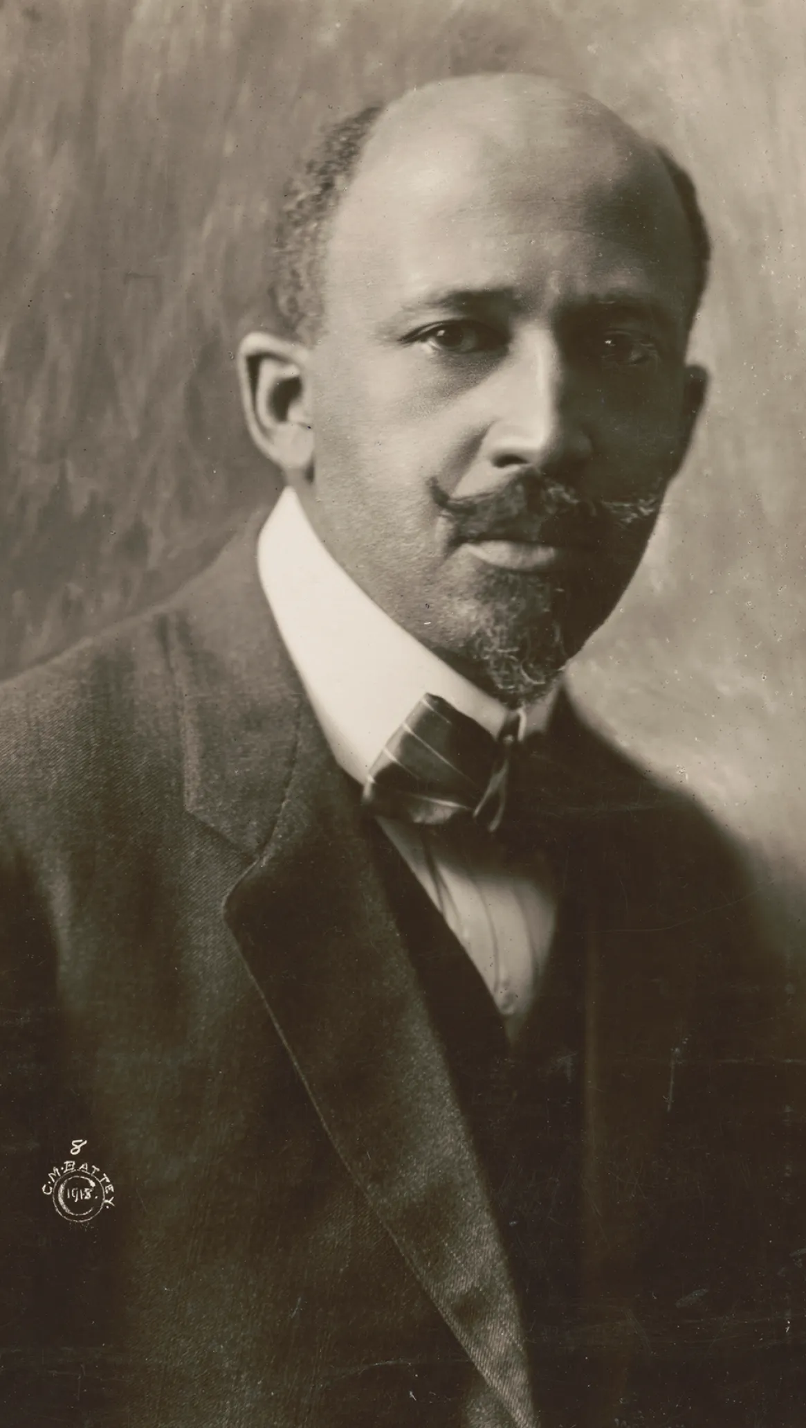 Portrait of W.E.B. Du Bois with a contemplative expression, dressed in a suit and bow tie, with a neatly trimmed mustache and goatee, looking slightly to the side.