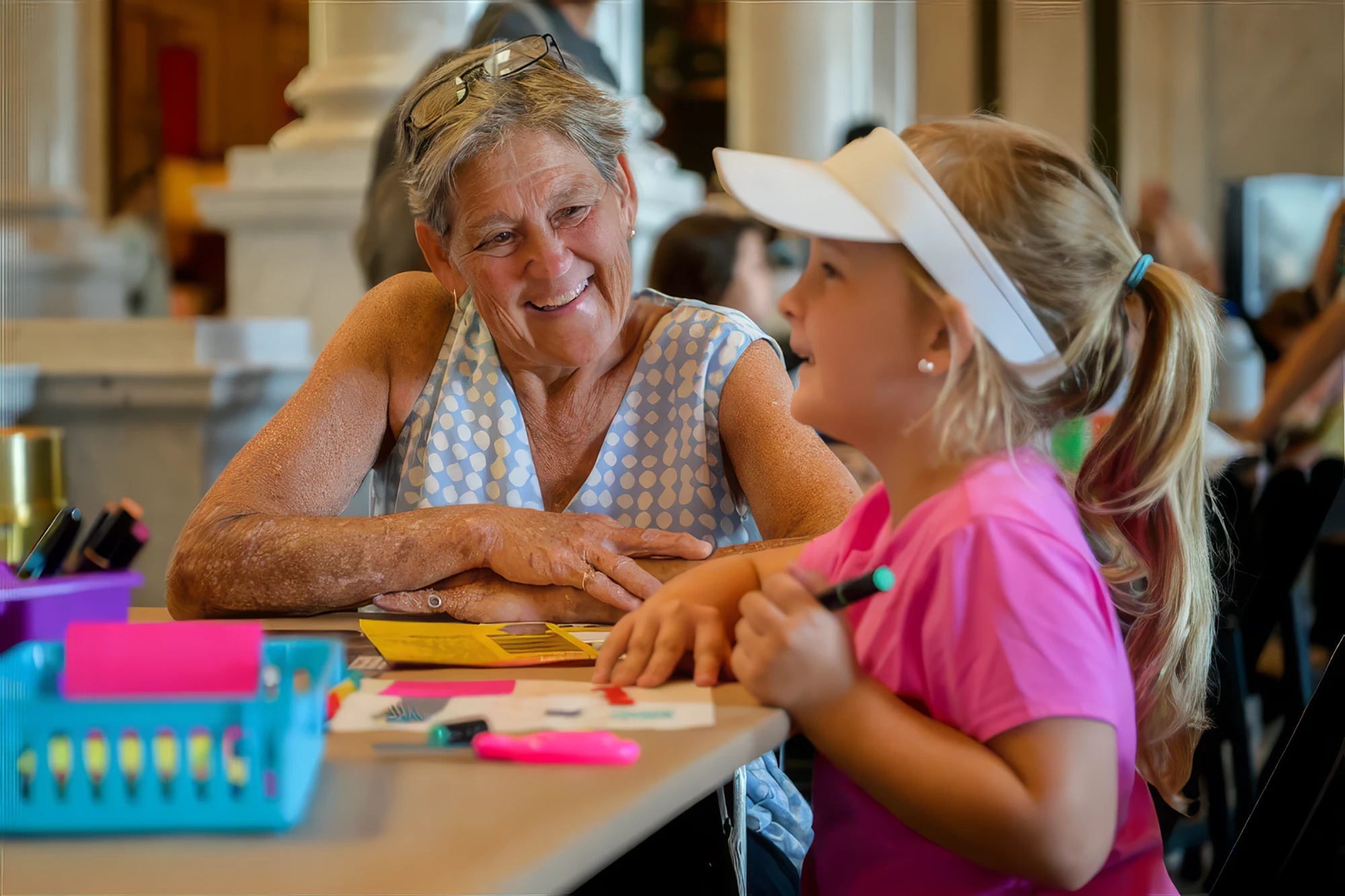 Woman smiles while talking with a young girl working on a craft project at a table